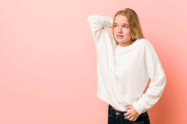 Jonge blonde tienervrouw wat betreft achterhoofd, denkend en het maken van een keuze.