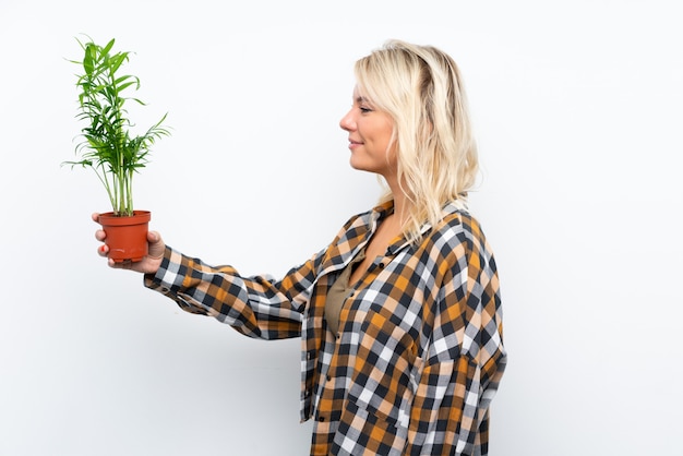 Jonge blonde tuinmanvrouw die een installatie over geïsoleerde witte achtergrond met gelukkige uitdrukking houden