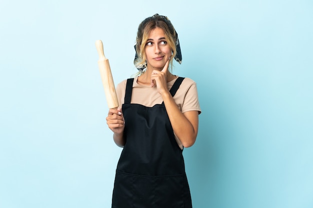 Jonge blonde Uruguayaanse kokende vrouw die op blauw wordt geïsoleerd dat twijfels heeft en denkt