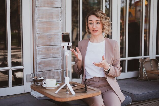 Jonge blonde vrouw blogger werkt in een straatcafé op een mobiele telefoon