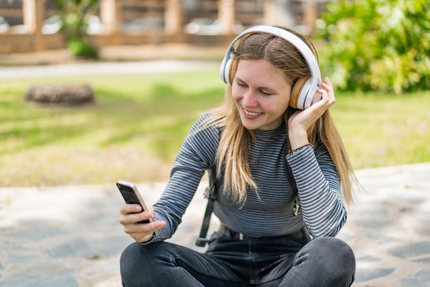 Jonge blonde vrouw buitenshuis met behulp van mobiele telefoon