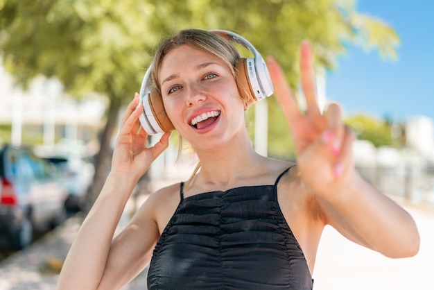 Jonge blonde vrouw die buiten muziek luistert en zingt