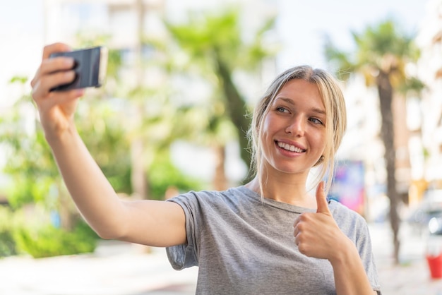 Jonge blonde vrouw die buitenshuis een selfie maakt met mobiele telefoon