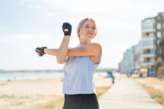 Jonge blonde vrouw die buitenshuis sport en stretching doet