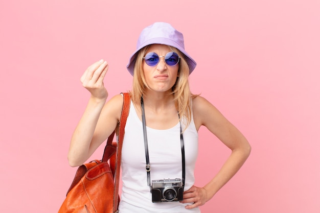 Jonge blonde vrouw die capice of geldgebaar maakt en zegt dat je moet betalen