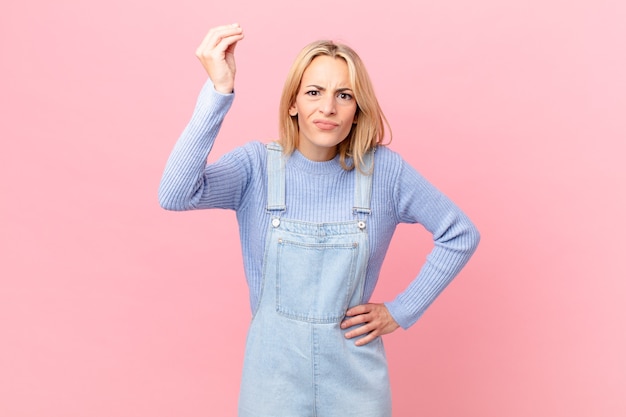 Jonge blonde vrouw die capice of geldgebaar maakt en zegt dat je moet betalen