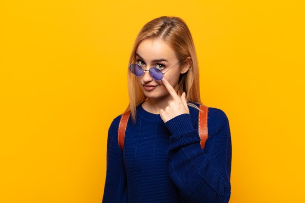 Jonge blonde vrouw die een oogje in het zeil houdt, niet vertrouwt, toekijkt en alert en waakzaam blijft