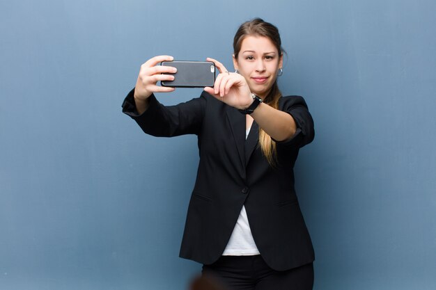 Jonge blonde vrouw die een smartphone op grungemuur gebruiken