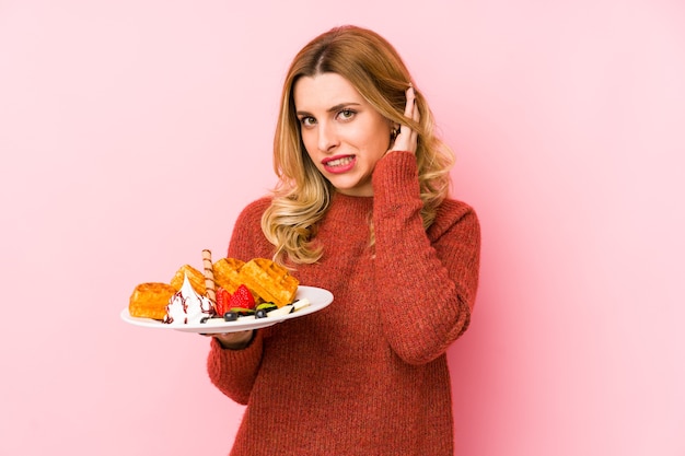 Jonge blonde vrouw die een wafeldessert eet geïsoleerde kegelvormige oren met handen.