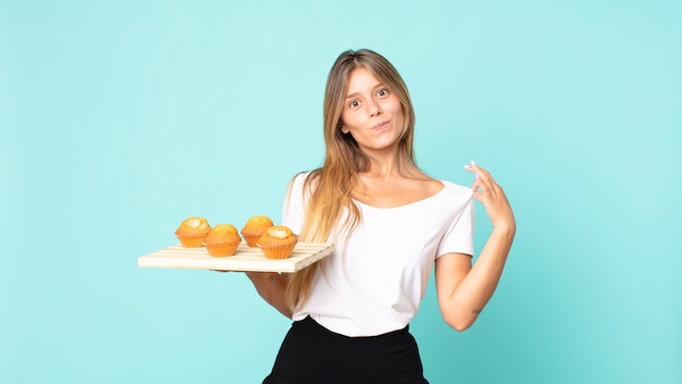 Jonge blonde vrouw die er arrogant, succesvol, positief en trots uitziet en een muffinstroy vasthoudt