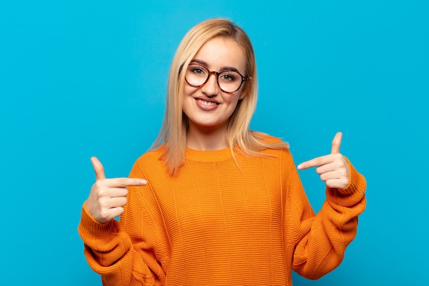 Jonge blonde vrouw die er trots, arrogant, blij, verrast en tevreden uitziet, naar zichzelf wijst en zich een winnaar voelt