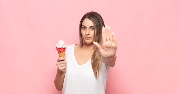 Jonge blonde vrouw die ernstig, streng, ontevreden en boos kijkt die open palm toont die stopgebaar maakt