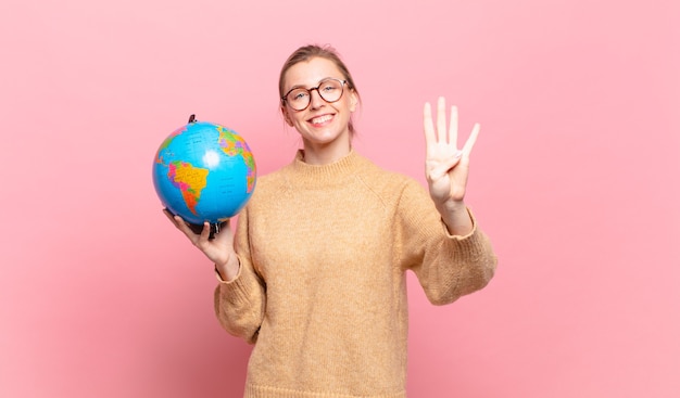 Jonge blonde vrouw die lacht en er vriendelijk uitziet, nummer vier of vierde toont met de hand naar voren, aftellend. wereld concept