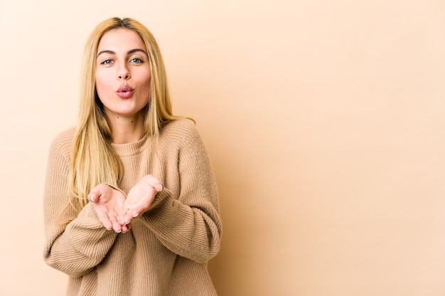 Foto jonge blonde vrouw die lippen vouwt en palmen houdt om luchtkus te verzenden