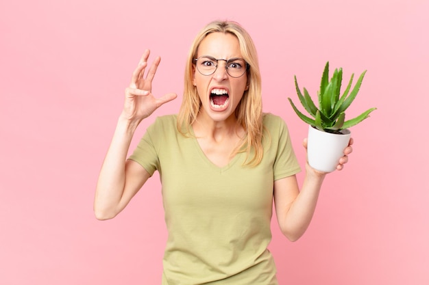 Jonge blonde vrouw die met de handen in de lucht schreeuwt en een cactus vasthoudt