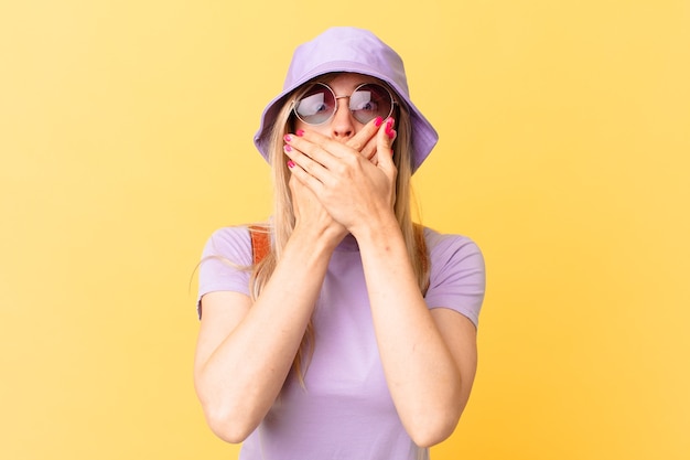 Jonge blonde vrouw die mond bedekt met handen met een geschokt