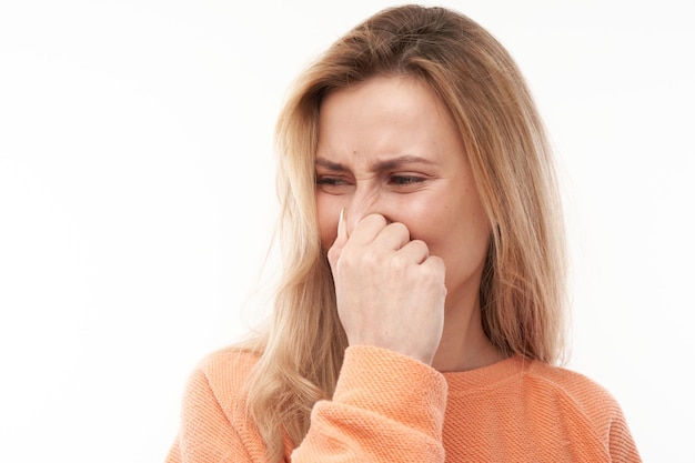 Jonge blonde vrouw die neus vasthoudt om walgelijke geur te vermijden, knijpt neus en mond met vingers en houdt adem in geïsoleerd op een witte achtergrond