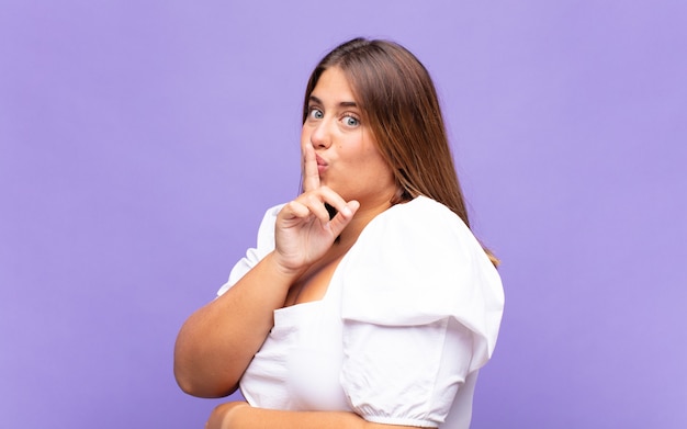 Jonge blonde vrouw die om stilte en stilte vraagt, met vinger voor mond gebaart, shh zegt of een geheim houdt