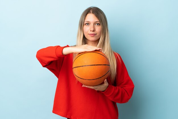 Jonge blonde vrouw die op blauw muur speelbasketbal wordt geïsoleerd