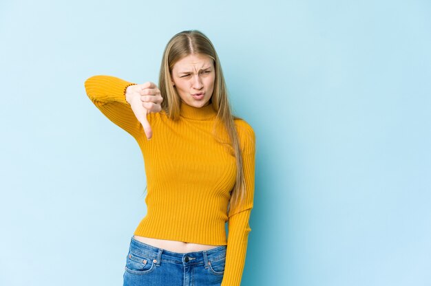 Jonge blonde vrouw die op blauwe muur wordt geïsoleerd die duim neer toont en afkeer uitdrukt