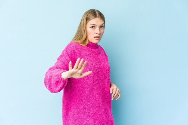 Jonge blonde vrouw die op blauwe muur wordt geïsoleerd die wegens een dreigend gevaar wordt geschokt