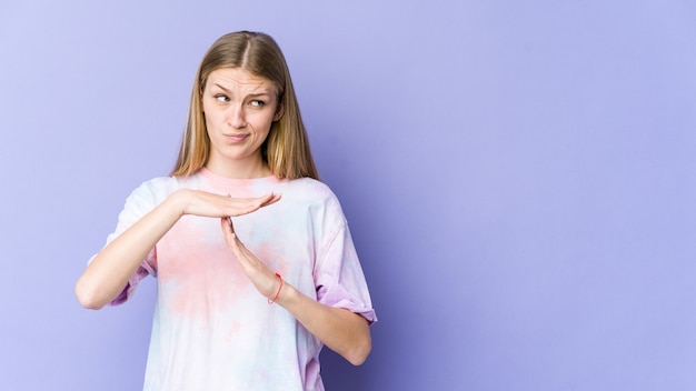 Jonge blonde vrouw die op purpere muur wordt geïsoleerd die een time-outgebaar toont.