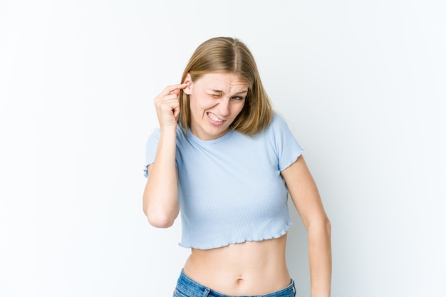 Jonge blonde vrouw die op witte muur wordt geïsoleerd die oren met handen behandelt.