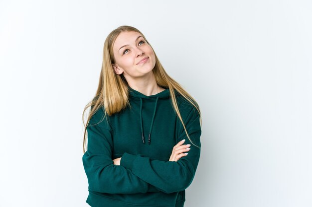 Jonge blonde vrouw die op witte muur wordt geïsoleerd die van het bereiken van doelstellingen en doeleinden droomt