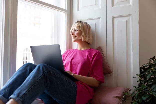 Foto jonge blonde vrouw die thuis op haar laptop werkt