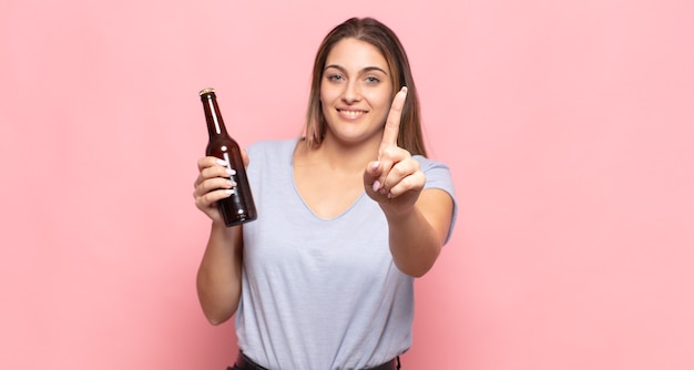 Jonge blonde vrouw die trots en zelfverzekerd glimlacht en nummer één triomfantelijk laat poseren, zich een leider voelt