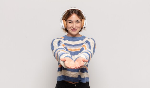 Jonge blonde vrouw die vrolijk lacht met een vriendelijke, zelfverzekerde, positieve blik, een object of concept aanbiedt en toont