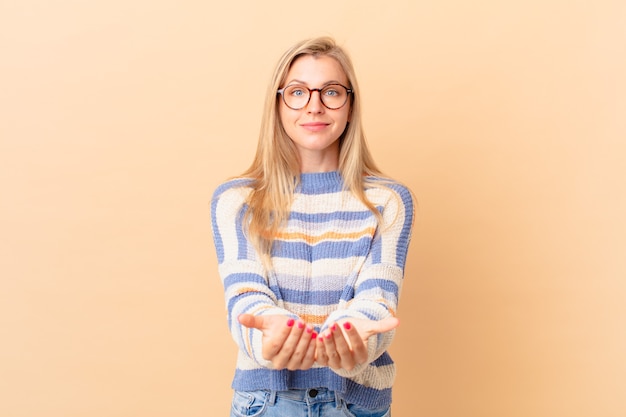 Jonge blonde vrouw die vrolijk lacht met vriendelijk en een concept aanbiedt en toont