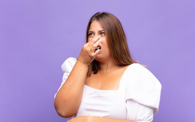 Jonge blonde vrouw die walgt en neus vasthoudt om te voorkomen dat ze een vieze en onaangename stank ruikt