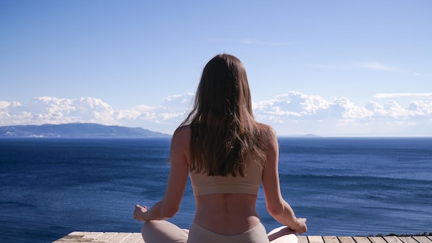 Foto jonge blonde vrouw die yoga doet zittend tegen zeezicht.