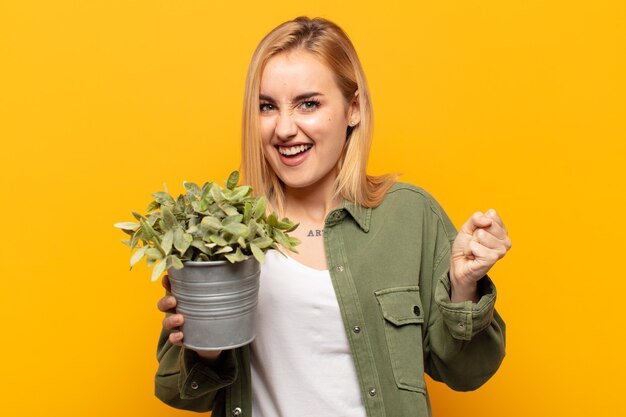 Jonge blonde vrouw die zich blij, verrast en trots voelt, schreeuwt en succes viert met een grote glimlach