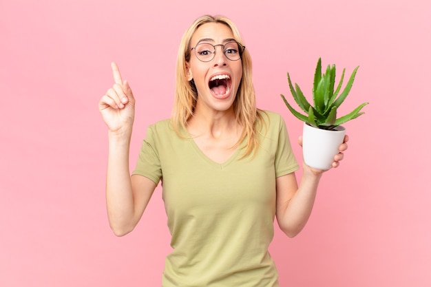 Jonge blonde vrouw die zich een gelukkig en opgewonden genie voelt na het realiseren van een idee en het vasthouden van een cactus