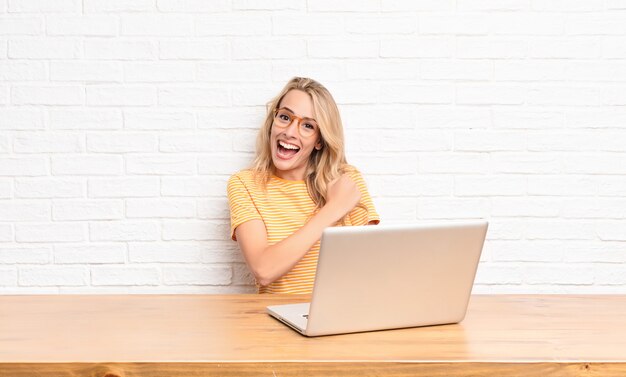 Jonge blonde vrouw die zich gelukkig, positief en succesvol voelt, gemotiveerd bij het aangaan van een uitdaging of het vieren van goede resultaten met behulp van een laptop