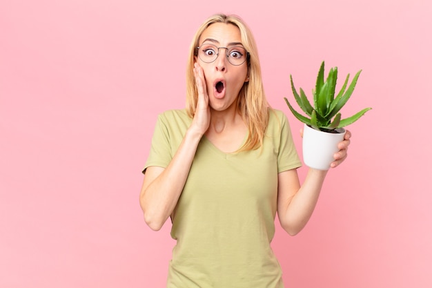 Jonge blonde vrouw die zich geschokt en bang voelt en een cactus vasthoudt