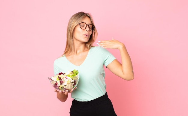 Jonge blonde vrouw die zich gestrest, angstig, moe en gefrustreerd voelt en een salade vasthoudt