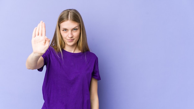 Jonge blonde vrouw die zich met uitgestrekte hand bevindt die stopbord toont