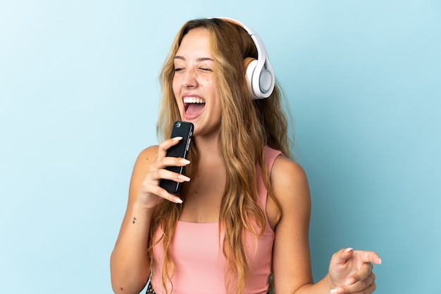 Jonge blonde vrouw geïsoleerd luisteren muziek met een mobiele telefoon en zingen