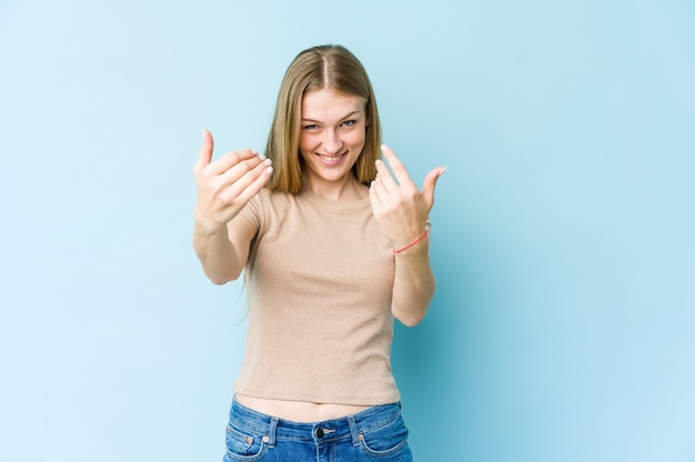 Jonge blonde vrouw geïsoleerd op blauw wijzend met vinger naar je alsof uitnodigend dichterbij komen.