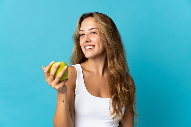 Jonge blonde vrouw geïsoleerd op blauwe muur met een appel