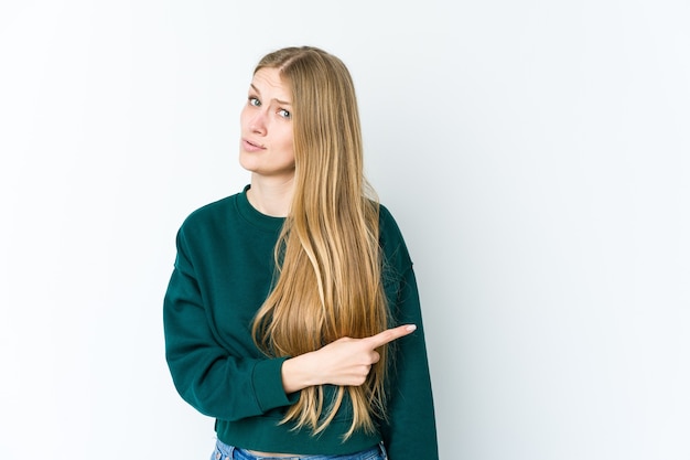 Jonge blonde vrouw geïsoleerd op een witte achtergrond glimlachend en opzij wijst, iets op lege ruimte tonen.