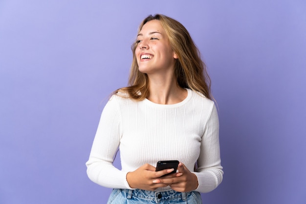 Jonge blonde vrouw geïsoleerd op paars met behulp van mobiele telefoon en opzoeken