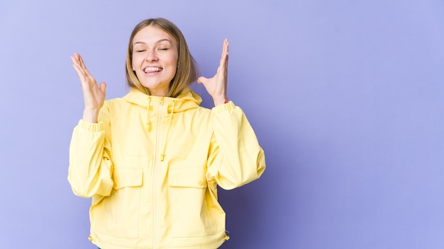 Jonge blonde vrouw geïsoleerd op paarse muur lacht hardop hand op de borst te houden