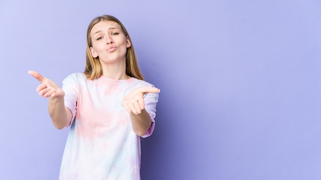 Jonge blonde vrouw geïsoleerd op paarse muur lippen vouwen en palmen vasthouden om luchtkus te sturen.