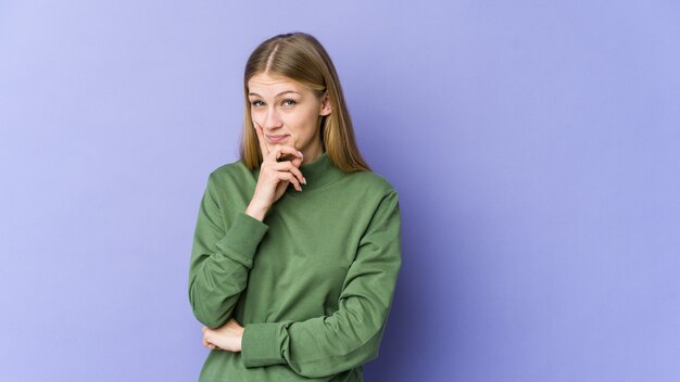 Jonge blonde vrouw geïsoleerd op paarse muur overweegt, een strategie plannen, na te denken over de manier van een bedrijf.