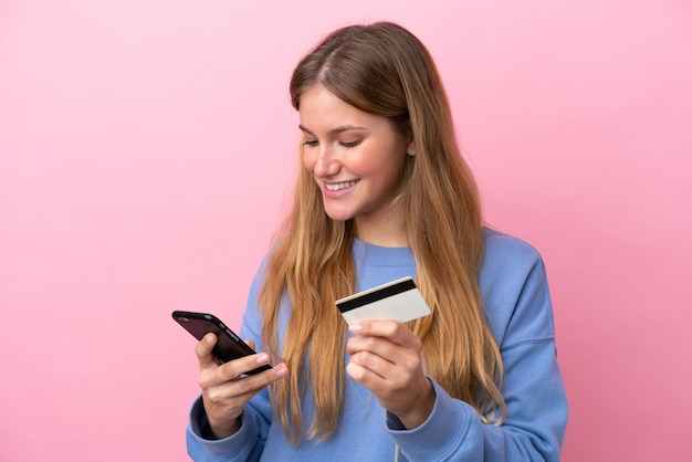 Jonge blonde vrouw geïsoleerd op roze achtergrond kopen met de mobiel met een creditcard