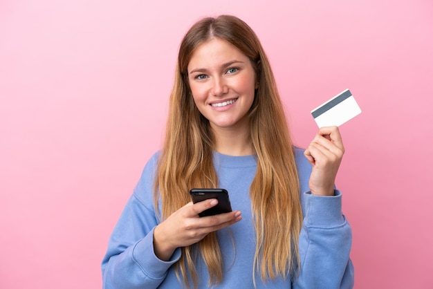 Jonge blonde vrouw geïsoleerd op roze achtergrond kopen met de mobiel met een creditcard